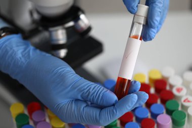 Eldivenli bir çalışan laboratuarda sıvı ile test tüpü tutuyor.