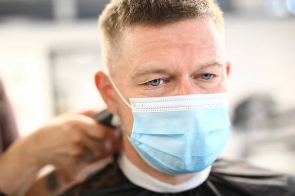 Man sits in protective medical mask at barbershop.