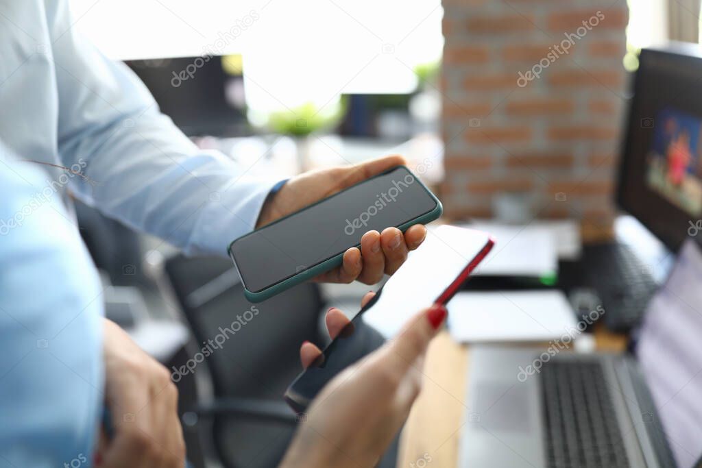 They hold two smartphones in their hands above desktop.