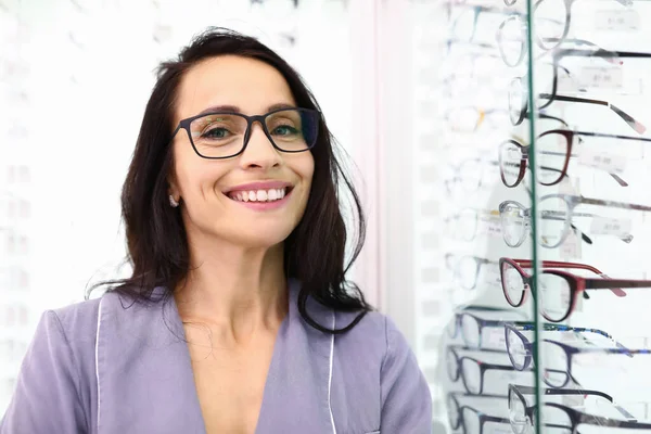 Mulher com óculos fica ao lado de uma vitrine com óptica. — Fotografia de Stock