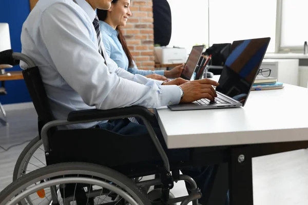 휠체어를 타고 사무실에서 노트북을 만드는 동료와 함께 일하는 남자. — 스톡 사진