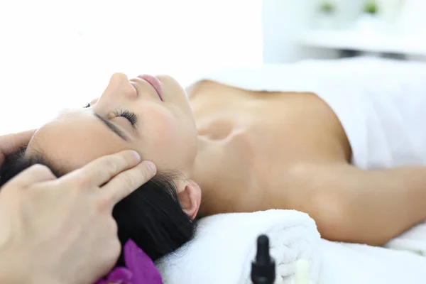 Woman lies on massage table with her eyes closed masseur does an acupressure face massage