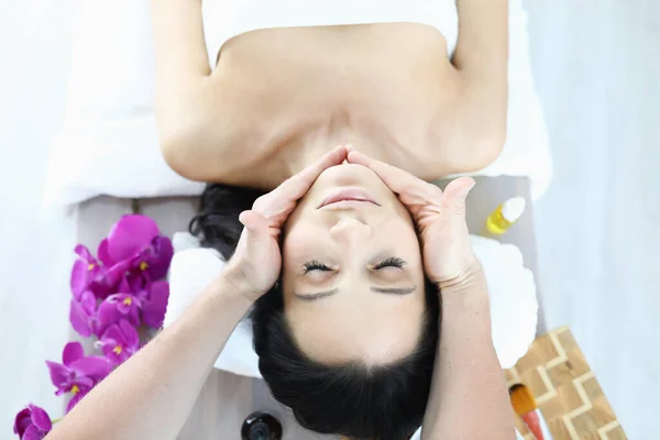 Vrouw ligt op massage tafel met haar ogen dicht, masseur houdt haar handen op de lijnen van de kin. — Stockfoto