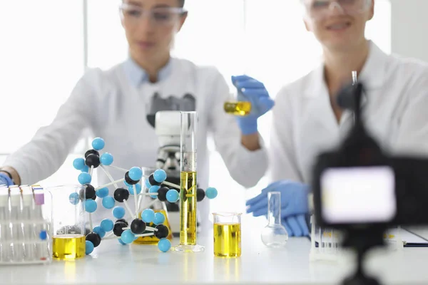 Ученые за рабочим столом, на котором фляжки и молекулы снимают эксперименты на видеокамеру — стоковое фото