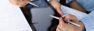 Erkek ve kadın eli, ofisindeki masada tükenmez kalemleri tabletin üzerinde tutuyor.