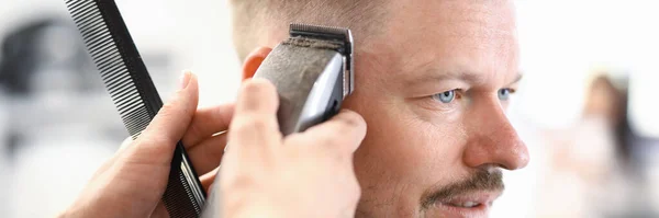 Jovem recebendo corte de cabelo com cortador e tesoura na barbearia retrato — Fotografia de Stock