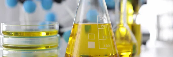 Вчений в гумових рукавичках тримає скляну колбу з жовтою рідиною в хімічній лабораторії крупним планом — стокове фото