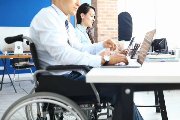 Man in wheelchair next to woman is sitting at desk and working — Stock Photo, Image