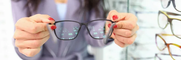 Les mains féminines tiennent des lunettes à monture noire à côté d'une vitrine d'optique — Photo