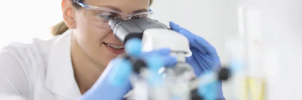 Frau mit Gummihandschuhen und chemischer Schutzbrille blickt im Laborporträt durchs Mikroskop — Stockfoto