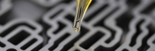 Dispenser pipette drips yellow liquid into automatic gearbox in chemical laboratory closeup