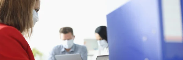Молодая женщина в деловом костюме и маске печатает на клавиатуре ноутбука в офисе с коллегами на заднем плане — стоковое фото