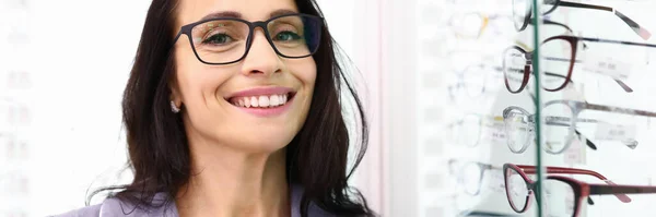 Kvinna med glasögon står bredvid ett skyltfönster med optik. — Stockfoto