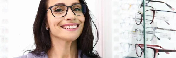 Woman with glasses stands next to a showcase with optics. — Stock Photo, Image