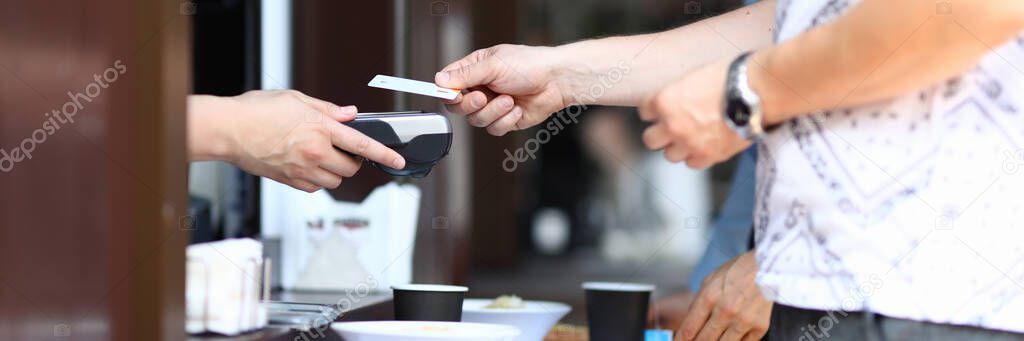 Man in coffee pays with credit bank card at terminal on tray with food