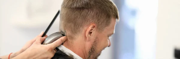 Man sits with his back master hairdresser cuts his hair with machine Stock Picture