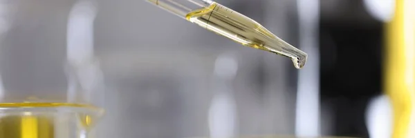 Yellow oil drips from test tube dispenser into the glass container.