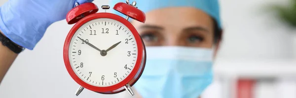 의료용 방호복을 입고 있는 의사가 손에 붉은 경보 시계를 들고 있다 스톡 사진