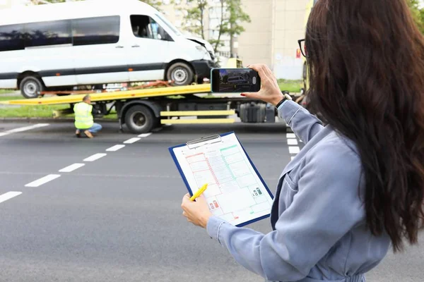 Kvinna med dokument i händerna tar bilder av förstörd bil på telefon — Stockfoto