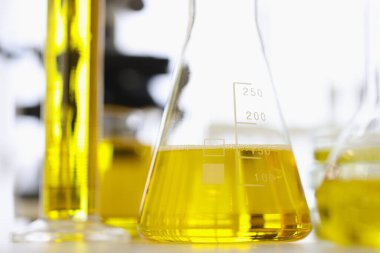 Test tüpleri ve sarı sıvılı mataralar kimya laboratuarının yakın çekim masasında duruyor.