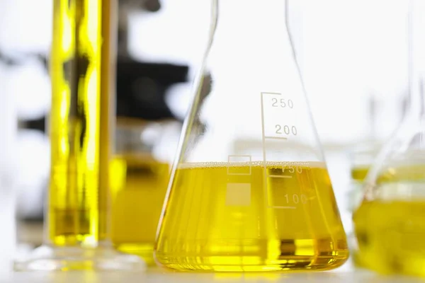 Zkušební zkumavky a baňky se žlutou kapalinou stojící na stole chemické laboratoře detailní — Stock fotografie