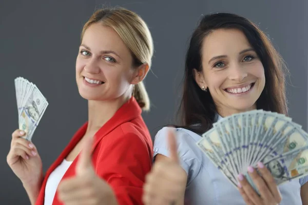 Two young women are holding dollars and showing thumbs up — Stock Photo, Image