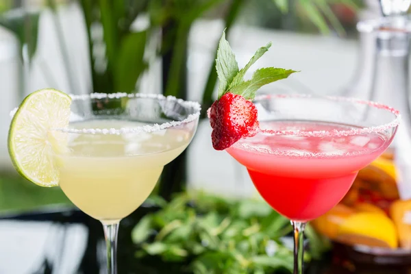 a mix of the two bright refreshing cocktails: lime daiquiri and strawberry daiquiri on a table in a restaurant with creative decoration of salt on the edge of the glass with fresh mint and lime slices
