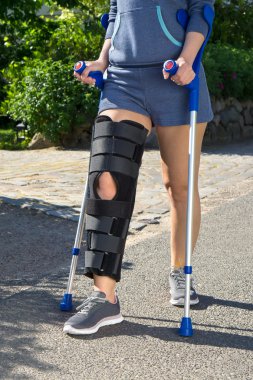 Woman wearing a leg brace walking on crutches. 