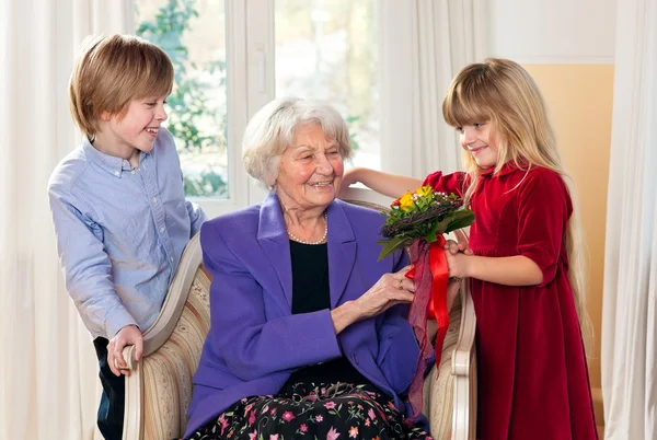 Nagymama fogadása virágok a unokák. — Stock Fotó