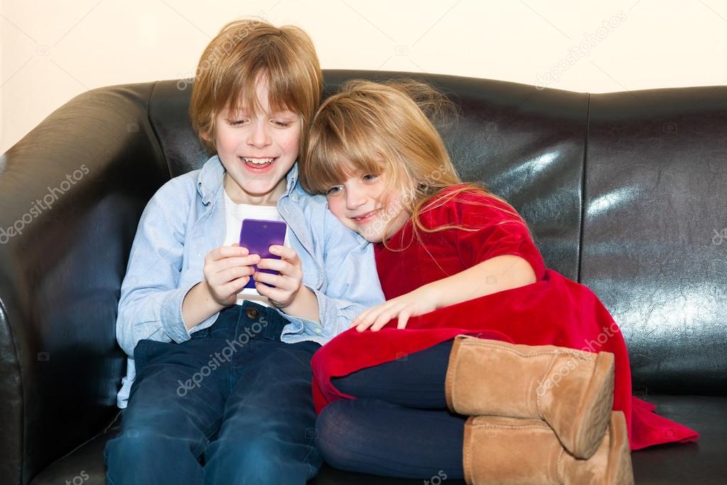 Two young children playing with a mobile phone.