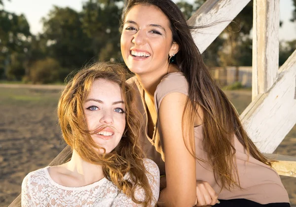 Amigos femininos sentados em escadas de madeira — Fotografia de Stock