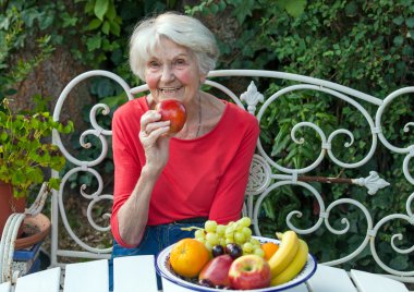 Senior woman in garden eating apple clipart