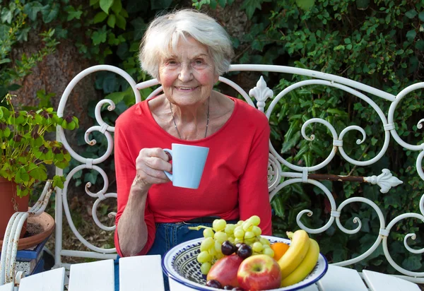 Äldre kvinna i trädgård dricka te — Stockfoto