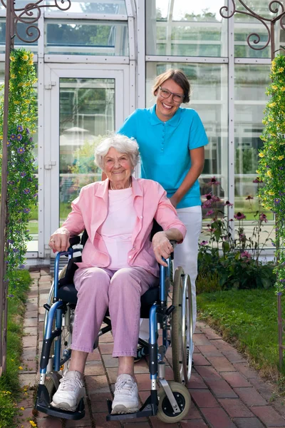 Femme âgée en fauteuil roulant avec assistant de soins — Photo
