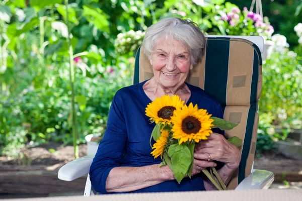 Mujer mayor en silla sosteniendo girasoles — Foto de Stock