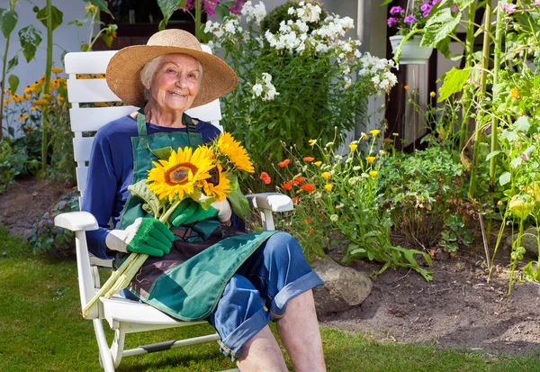 Senior vrouw op stoel bedrijf zonnebloemen — Stockfoto