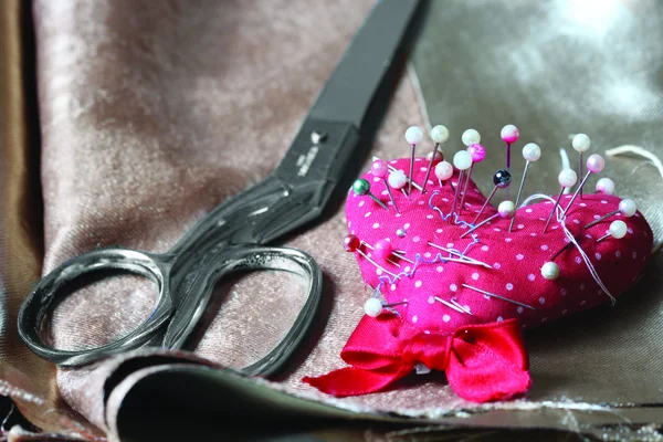 Metal scissors and pin on brown fabric — Stock Photo, Image