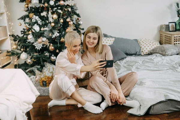 Blonde women at home take a selfie on the background of a Christmas tree. The concept of friendship and relationships. LGBT PERSON