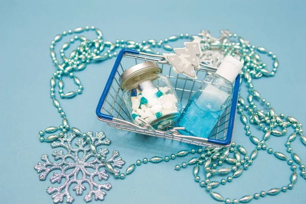 Pills in a jar, antiseptic hand gel and Christmas decorations in a shopping basket on a blue background. Christmas gifts in the age of coronavirus. Christmas sales, purchases and discounts. — Stock Image Pills in a jar, antiseptic hand gel and Christmas decorations in a shopping basket on a blue background. Christmas gifts in the age of coronavirus. Christmas sales, purchases and discounts. Stock Image
