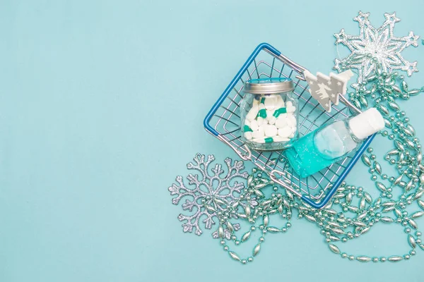 Pills in a jar, antiseptic hand gel and Christmas decorations in a shopping basket on a blue background. Christmas gifts in the age of coronavirus. Christmas sales, purchases and discounts. Copy spase. — Stock Image Pills Jar Antiseptic Hand Gel Christmas Decorations Shopping Basket Blue Royalty Free Stock Images