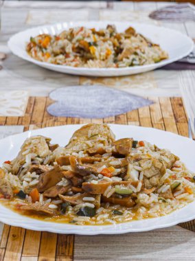 Et ve sebzeli bir tabak pirinç. Pirinç kahverengi ve et kahverengidir. Sebzeler turuncu ve yeşil.