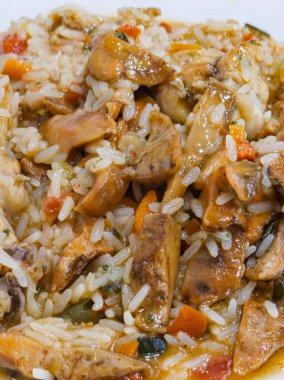 Et ve sebzeli bir tabak pirinç. Pirinç kahverengi ve et kahverengidir. Sebzeler turuncu ve yeşil.