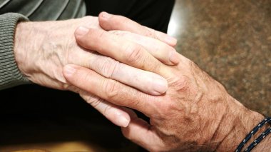 Bir adam ve yaşlı bir adam el ele tutuşuyor. Sahne sıcak, rahatlatıcı ve sevgiyi ve anlayışı yansıtıyor..