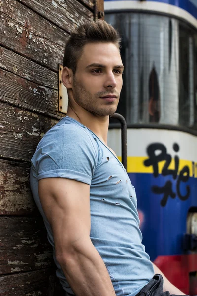 Young man sitting against old wood wall — Stock Photo, Image