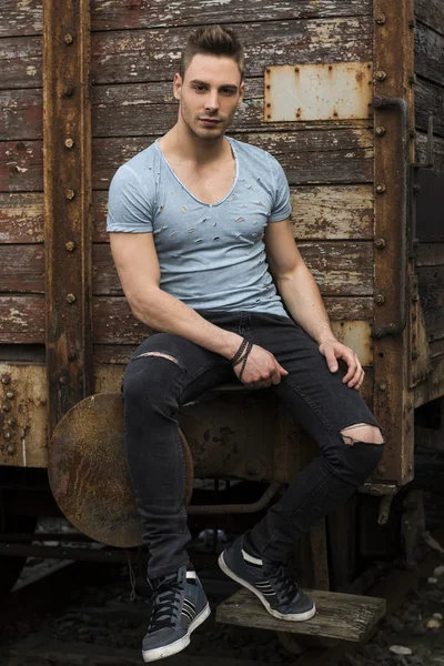 Young man sitting against old rusty train — Stock Photo, Image