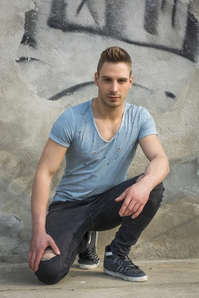 Красивый молодой человек сидит на бетоне в разорванных джинсах — стоковое фото