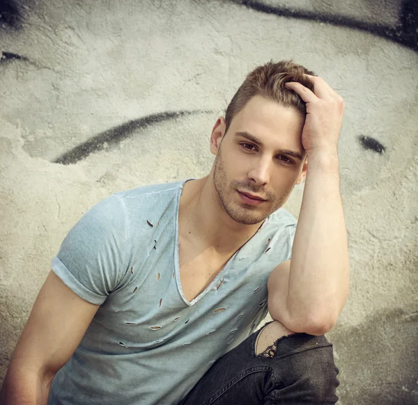 Handsome young man with ripped jeans sitting outdoor — Stock Photo, Image