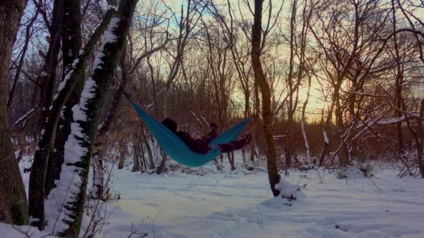 人躺在冬天森林里的树下的吊床上 男人放松 冬季露营 — 图库视频影像