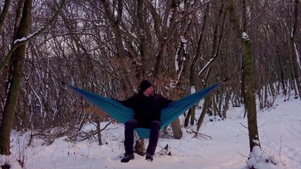 冬の森の木の下のハンモックに寝そべってる男 リラックスした男 冬のキャンプ — ストック動画