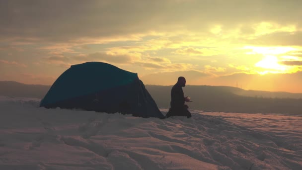 雪に覆われた冬の山の中でテントの前で一日のハイキングの後に食べるハイカー リラックスした — ストック動画